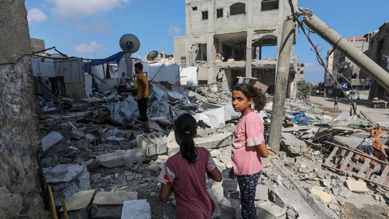 Two Palestinian girls and two men inspect a destroyed home in Magazi refugee camp, in the central Gaza Strip, following an Israeli air strike (14 August 2024)