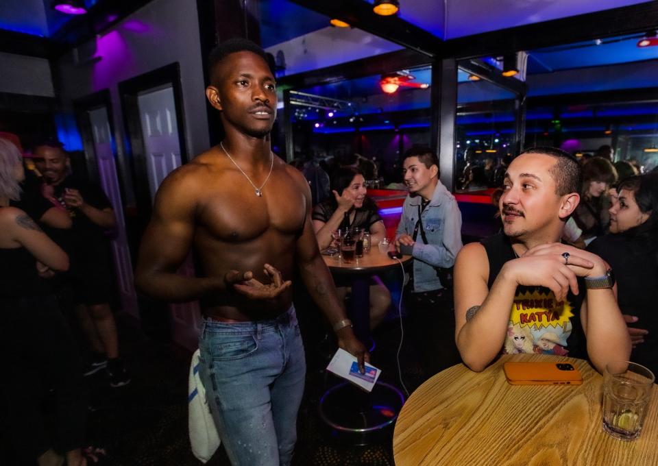 A shirtless man walks among people seated at tables.