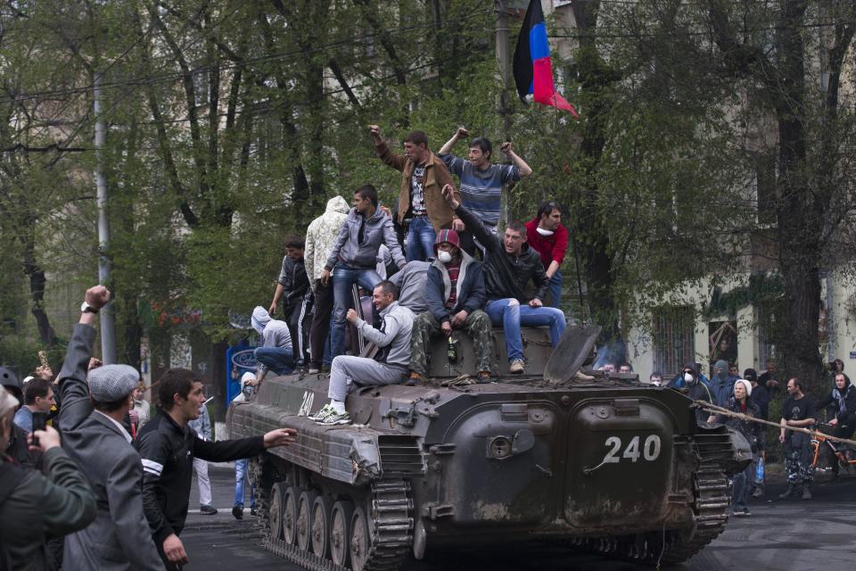 People greet pro-Russian activists atop of a government forces armored personal carrier captured from the enemy in fighting in Mariupol, eastern Ukraine, Friday, May 9, 2014. Fighting exploded Friday in Mariupol, a city of 500,000 on the Sea of Azov that is on the main road between Russia proper and Crimea. The fighting between government forces and insurgents in Mariupol has left several people dead. (AP Photo/Alexander Zemlianichenko)