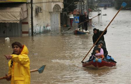 A member of the Palestinian civil defense paddles a boat as he evacuates a man and his children after their house was flooded with rainwater on a stormy day in the northern Gaza Strip December 14, 2013. REUTERS/Mohammed Salem