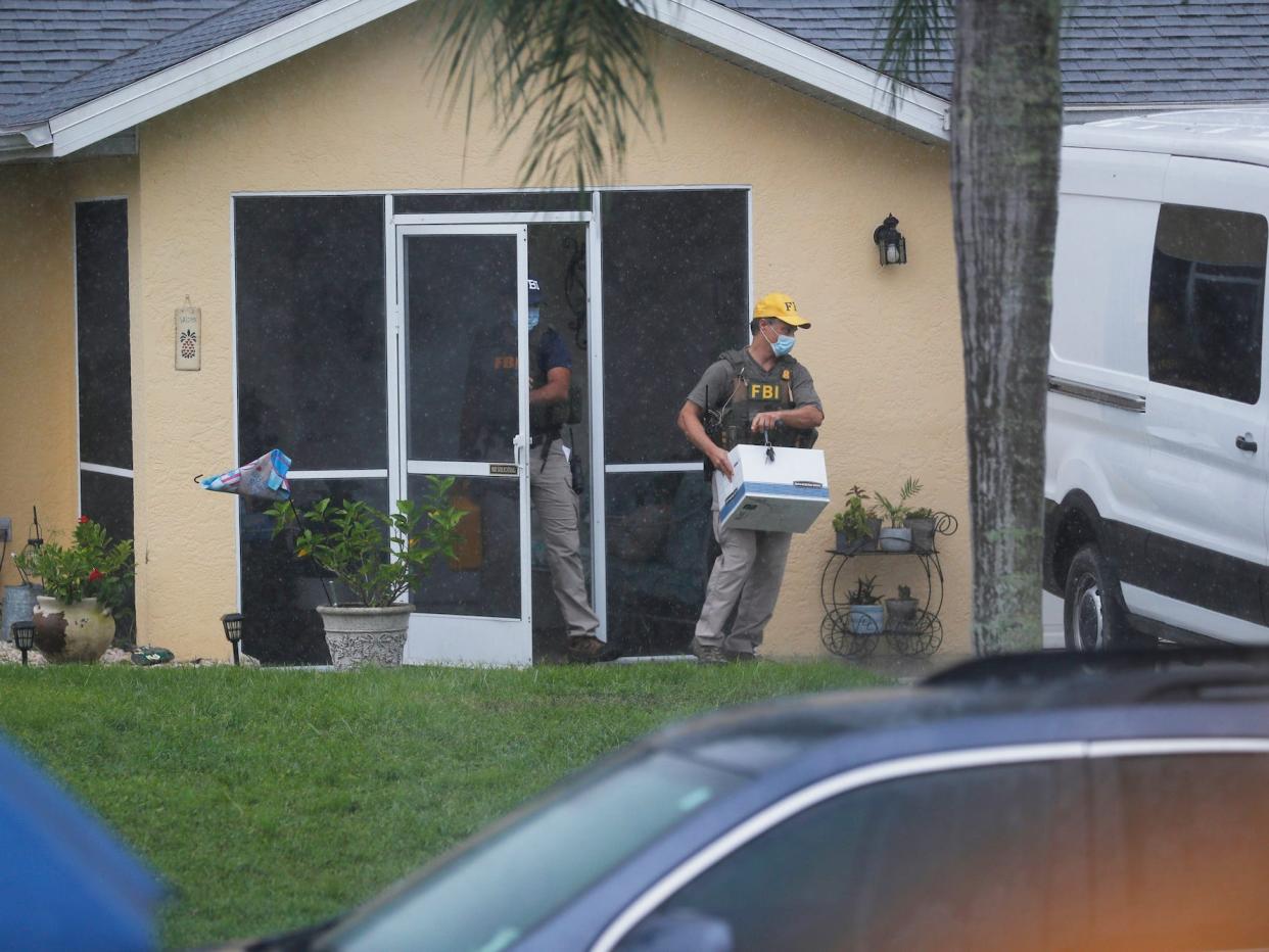 An FBI agent walks out of the door of the house with a box