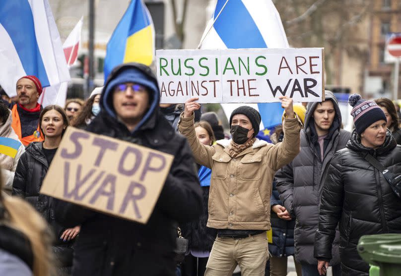 Un hombre en una marcha de paz sostiene un cartel con el lema "Los rusos están contra la guerra" cerca del Consulado de Rusia acordonado por la policía en Alemania. en 2022.