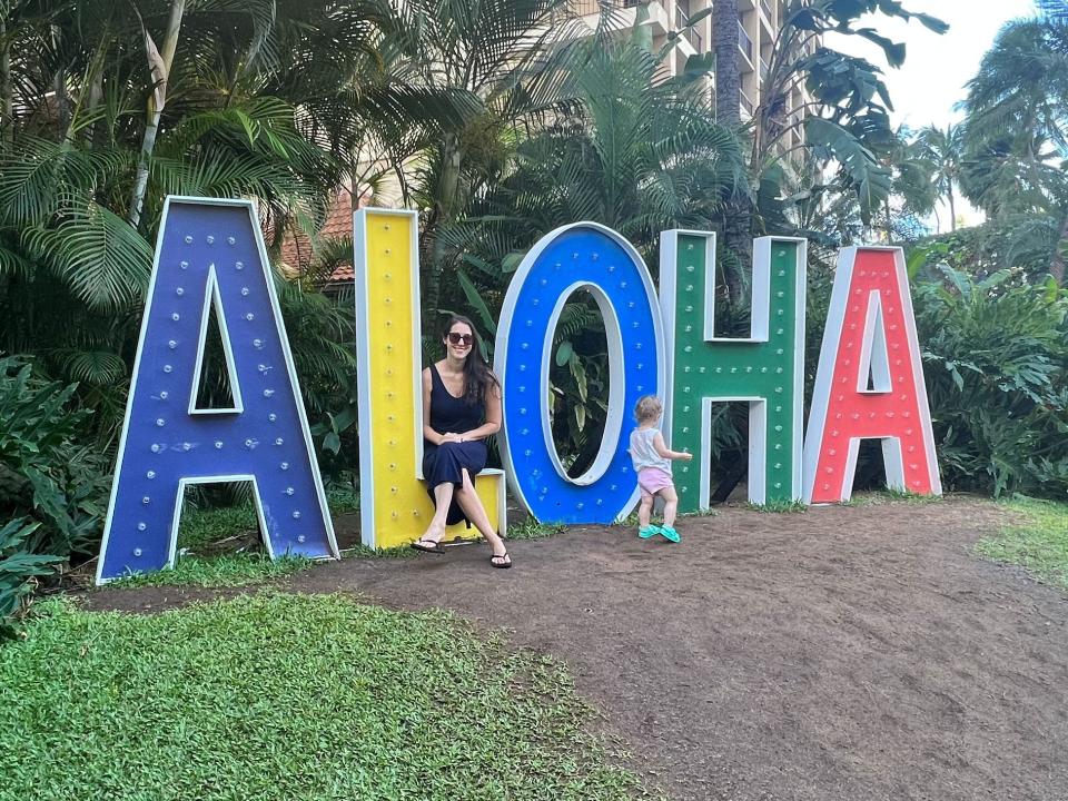 A woman and her child sitting on a lifesize colorful Aloha sign.