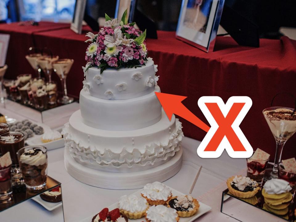 A dessert table filled with pastries and a wedding cake with pink flowers on top and white frosting with a red arrow and X pointing to it