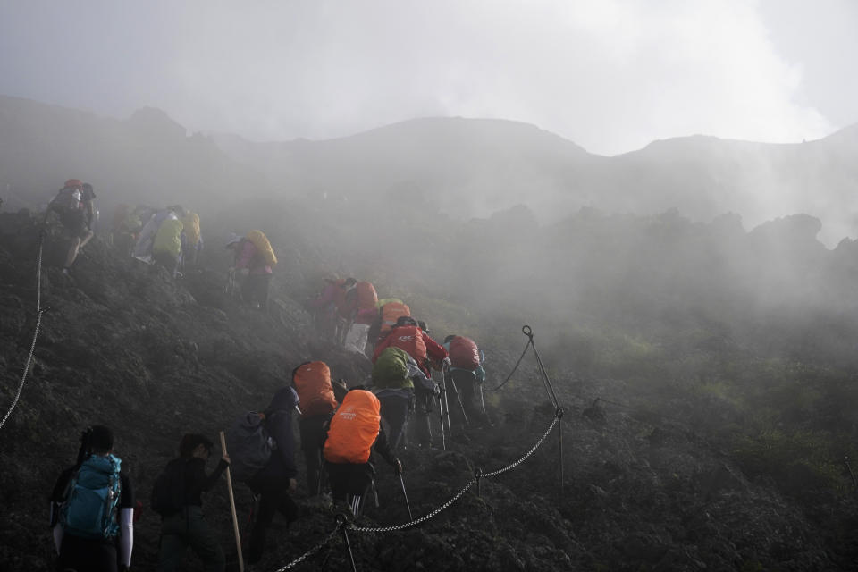 People climb through a dense fog as they make their way along the Yoshida trail towards the summit of Mount Fuji, Monday, Aug. 26, 2019, in Japan. The Yoshida trail is the easiest and most popular among the climbing routes, with climbers wearing headlamps and carrying heavy packs spaced just feet apart on the rugged, rocky terrain. (AP Photo/Jae C. Hong)