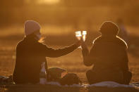 Women toast during a sunset at Cruzeiro Square in Brasilia, Brazil, Friday, July 31, 2020. People gathered in the late afternoon as authorities eased the restrictions related to the new coronavirus, despite that Brazil's official COVID-19 death toll is the second highest in the world after the United States. (AP Photo/Eraldo Peres)