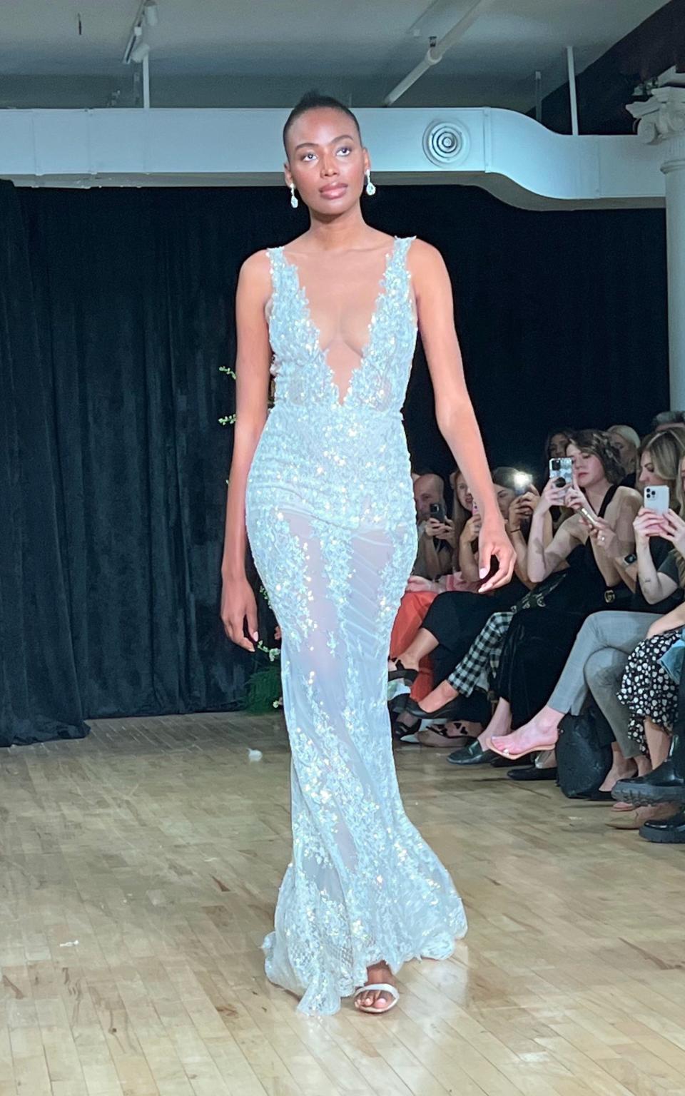 A woman walks down a runway in a low cut wedding dress.