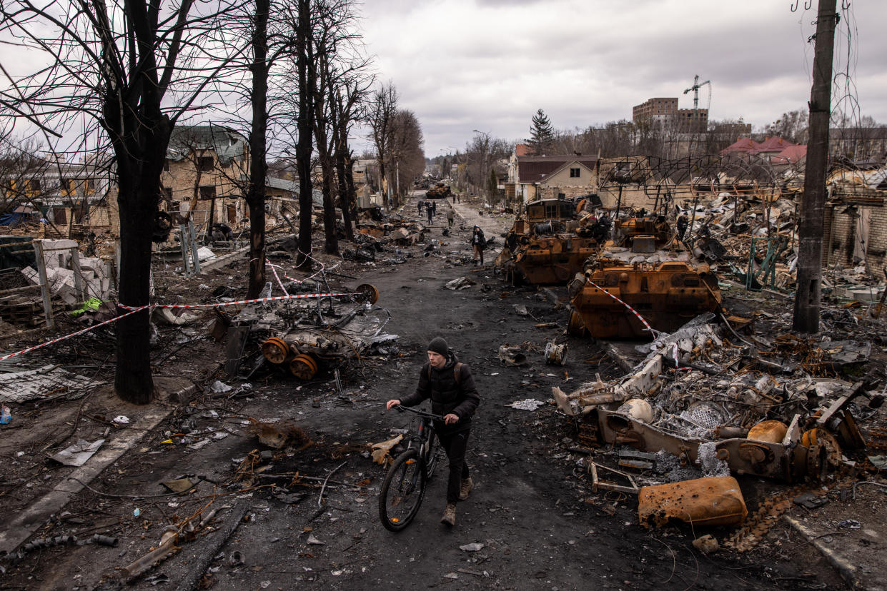 A man walks his bike past debris and destroyed Russian military vehicles on a Ukraine street.