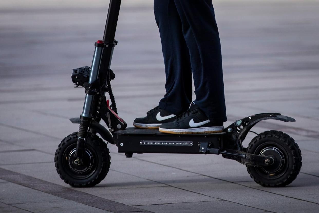 A person rides an electric kick scooter in Vancouver. E-scooters have proliferated across B.C., but provincial laws governing them have yet to allow the devices in most municipalities. (Ben Nelms/CBC - image credit)