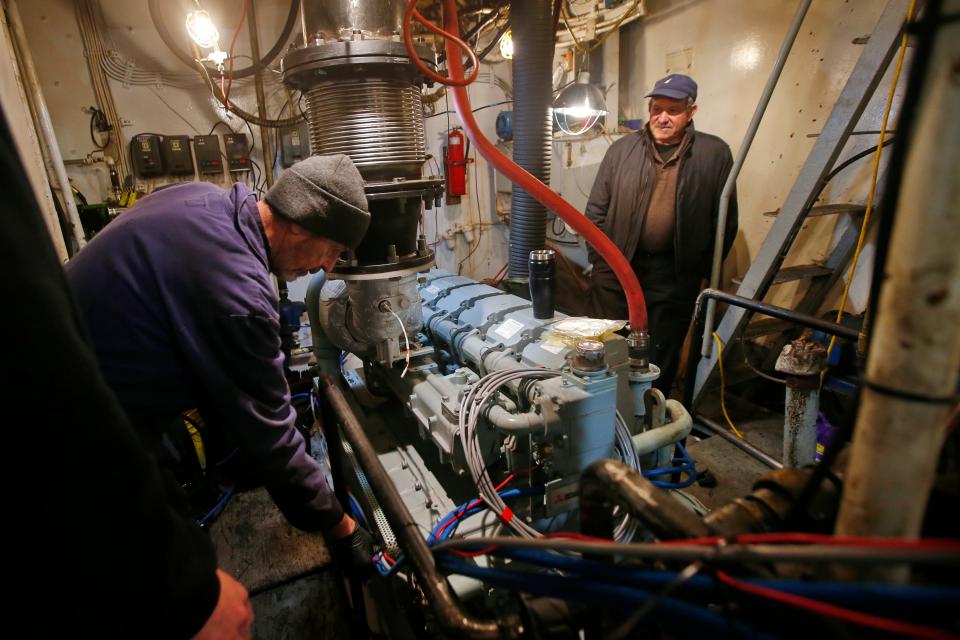 Pedro Cura, owner of the fishing boat Fisherman, looks on as Robert Savage a technician with Windward Power Systems installs the wiring for the new engine they are installing in the hull of the New Bedford fishing boat.