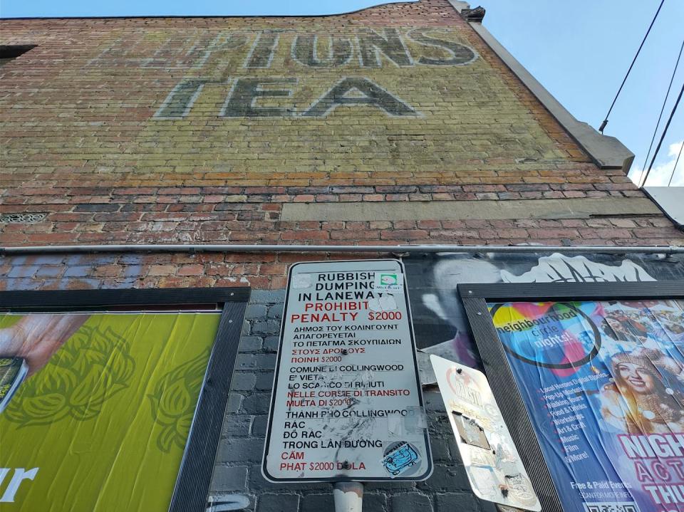 A faded mural advertisement (ghost sign), municipal signs covered in stickers, framed street posters and faded graffiti tags occupy shared surfaces, demonstrating visual justice through the presence of multiple voices. Sabina Andron