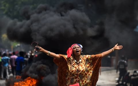 A demonstrator holds up her arms and chants slogans during a protest against the ruling government in Port-au-Prince in June - Credit: CHANDAN KHANNA/AFP/Getty Images