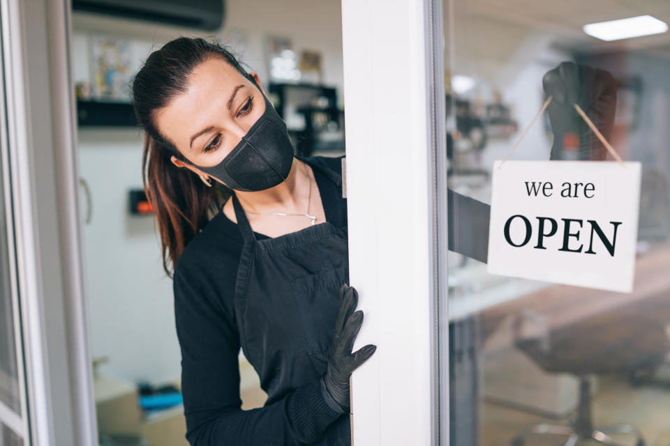 Happy business owner hanging an open sign during COVID-19 (Getty Images)