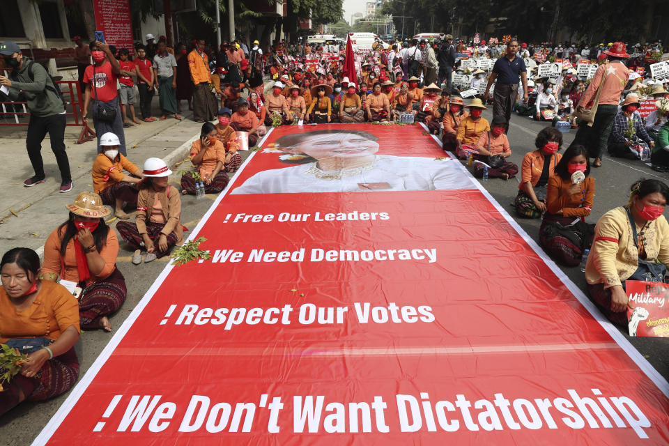 Protesters sit next to a giant banner with images of ousted leader Aung San Suu Kyi during an anti-coup protest in Mandalay, Myanmar, Sunday, Feb. 21, 2021. Police in Myanmar shot dead a few anti-coup protesters and injured several others on Saturday, as security forces increased pressure on popular revolt against the military takeover. (AP Photo)