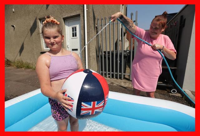 Danielle Lofthouse cools down her daughter Amelia Bradford, 10, with a hose as they enjoy the hot weather off the Shankill Road in Belfast (Liam McBurney/PA) (PA Media)