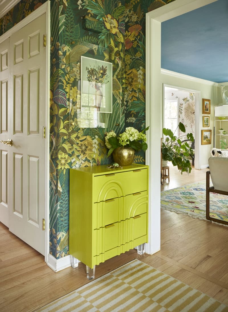 Small lime green storage unit against wall lined with bold botanical green wallpaper.