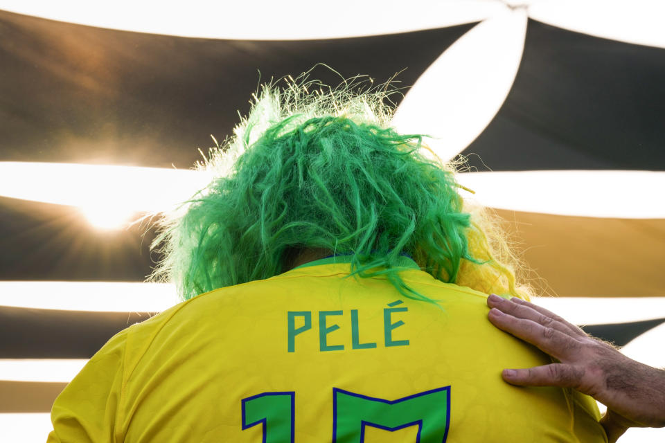 A man puts his hand on the shoulder of a fan wearing a shirt in support of Pelé at a Brazilian fan party before the the World Cup round of 16 soccer match between Brazil and South Korea, in Doha, Dec. 5, 2022. The 82-year-old Pelé remained in a hospital in San Paulo recovering from a respiratory infection that was aggravated by COVID-19, but the news coming from Brazil early Monday was good. (AP Photo/Ashley Landis)