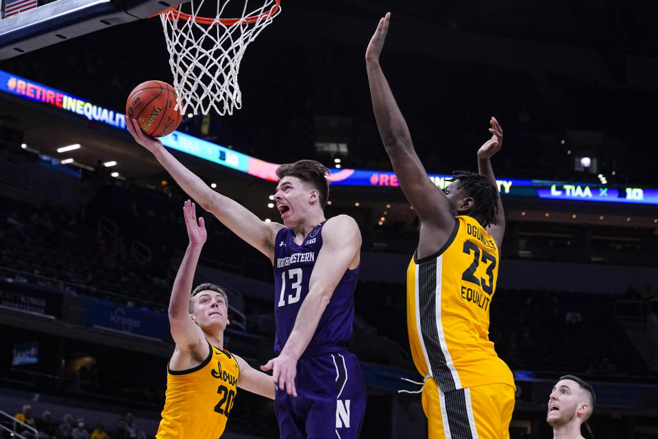 Northwestern guard Brooks Barnhizer (13) shoots between Iowa guard Payton Sandfort (20) and forward Josh Ogundele (23) in the second half of an NCAA college basketball game at the Big Ten Conference tournament in Indianapolis, Thursday, March 10, 2022. Iowa defeated Northwestern 112-76. (AP Photo/Michael Conroy)