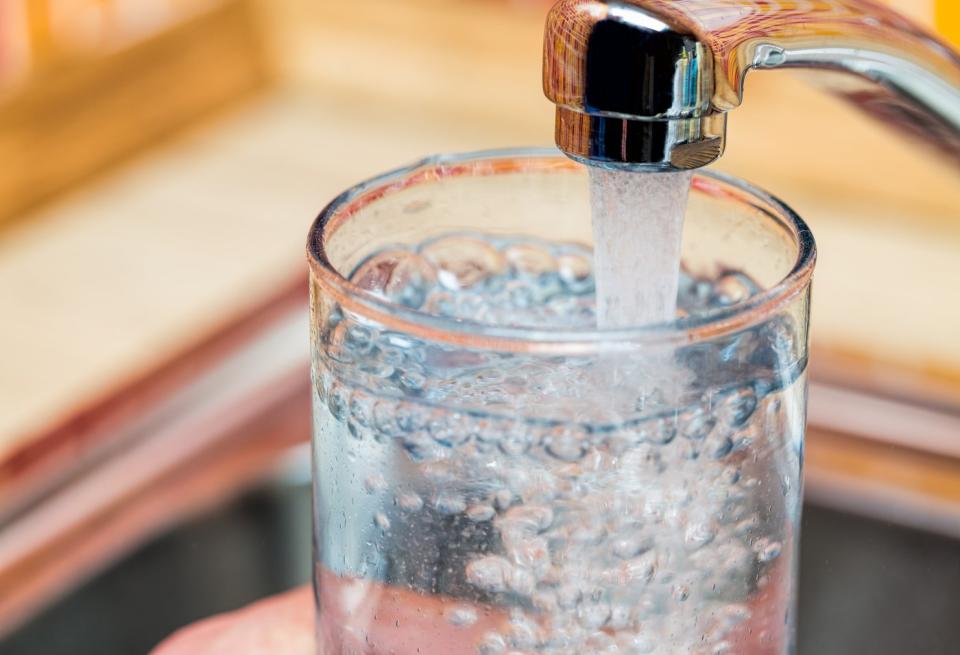 A person filling a glass with water using a kitchen tap.