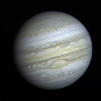 faint jupiter in yellow white and brown hanging in black space