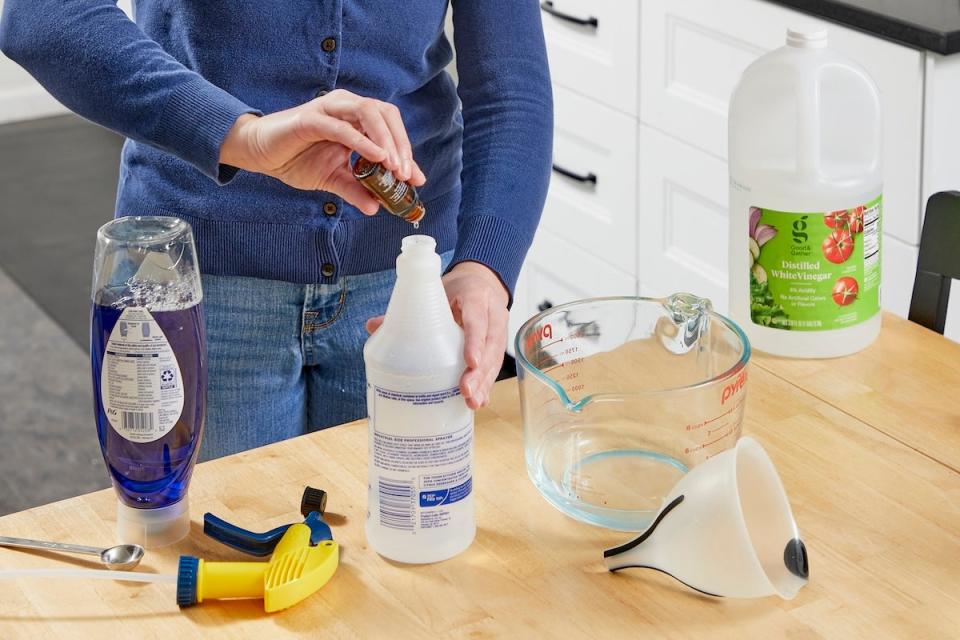 A person adding essential oil drops to a spray bottle to make homemade window cleaner for the house.