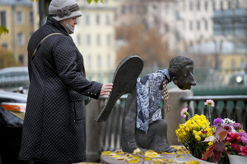 A woman touches the sculpture 'Sad Angel', a memorial for St. Petersburg's medical workers who died from coronavirus during their work in St. Petersburg, Russia, Friday, Oct. 15, 2021. Russia's daily tolls of coronavirus infections and deaths have surged to another record in a quickly mounting figure that has put a severe strain on the country's health care system. The record for daily COVID-19 deaths in Russia has been broken repeatedly over the past few weeks as fatalities steadily approach 1,000 in a single day. (AP Photo/Dmitri Lovetsky)