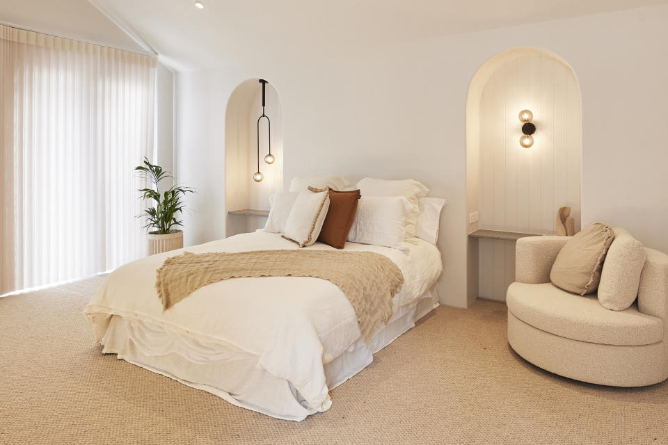 A bed in the centre, a chair to the right and a potted plan by the window on the left. Cream tones throughout. 