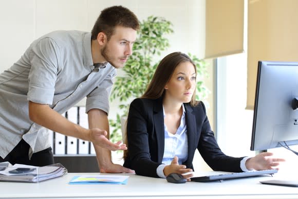 Two young bueinesspeople spread their hands in confusion over what they see on a shared computer screen.