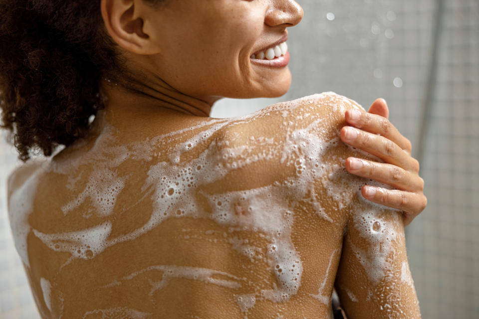 Person smiling in a shower, seen from behind, covered in soap suds. The image conveys a sense of cleanliness and personal care