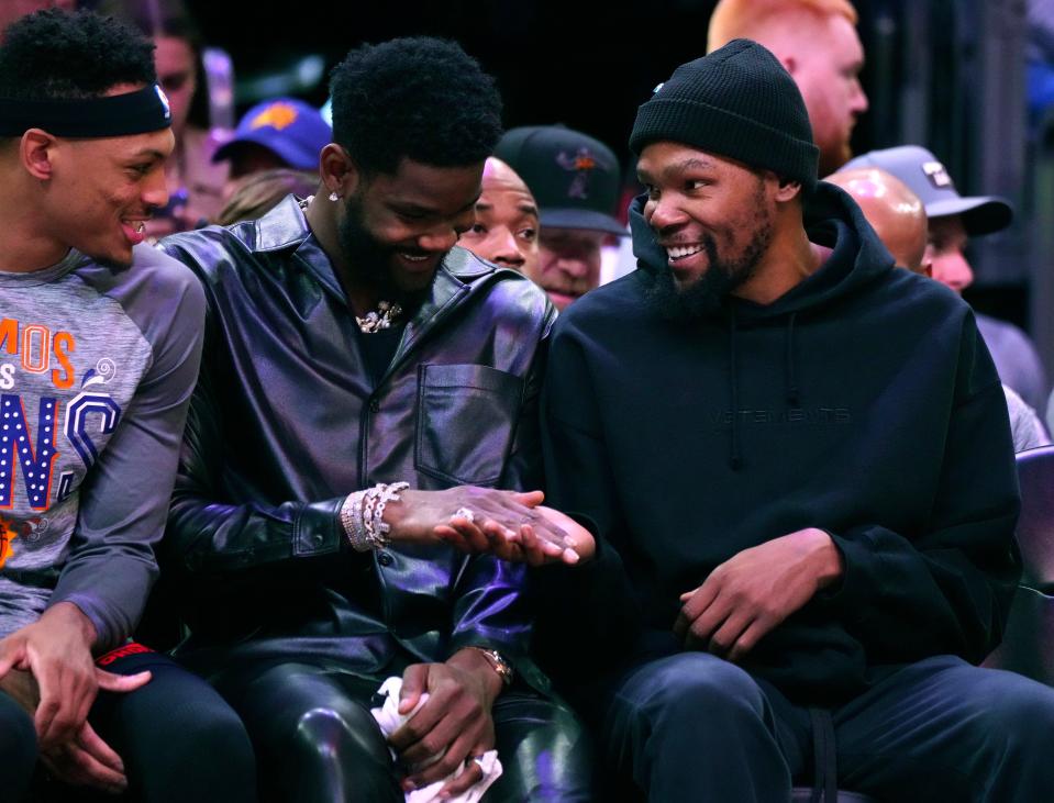 Suns center Deandre Ayton (left) and forward Kevin Durant high-five on the bench during a game against the 76ers at Footprint Center in Phoenix on March 25, 2023.