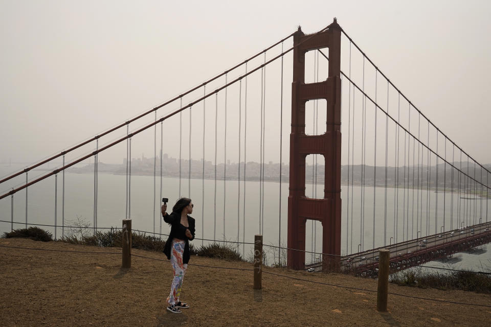 A woman takes a selfie as smoke from wildfires obscures the Golden Gate Bridge and San Francisco skyline in the background near Sausalito, Calif., Wednesday, Aug. 18, 2021. Wind-driven wildfires raged Wednesday through drought-stricken forests in the mountains of Northern California after incinerating hundreds of homes and forcing thousands of people to flee to safety. (AP Photo/Eric Risberg)