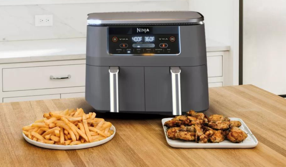 a ninja air fryer on a table with plates of french fries and chicken wings