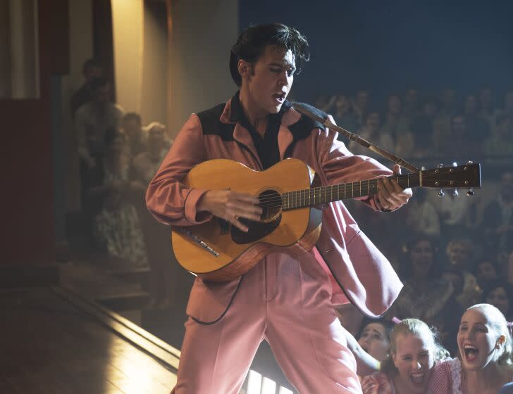 Austin Butler wearing a pink suit and holding a guitar on stage