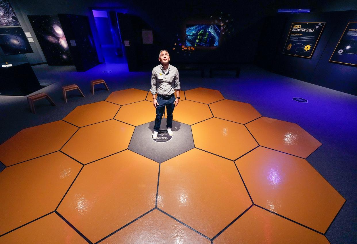 Seth Mayo, curator of science, stands in the "Unfolding the Universe: The James Webb Space Telescope" exhibit at Museum of Arts and Sciences in Daytona Beach on Thursday, May 25, 2023. Mayo is standing in the middle of an image on the floor depicting the telescope's primary mirror.