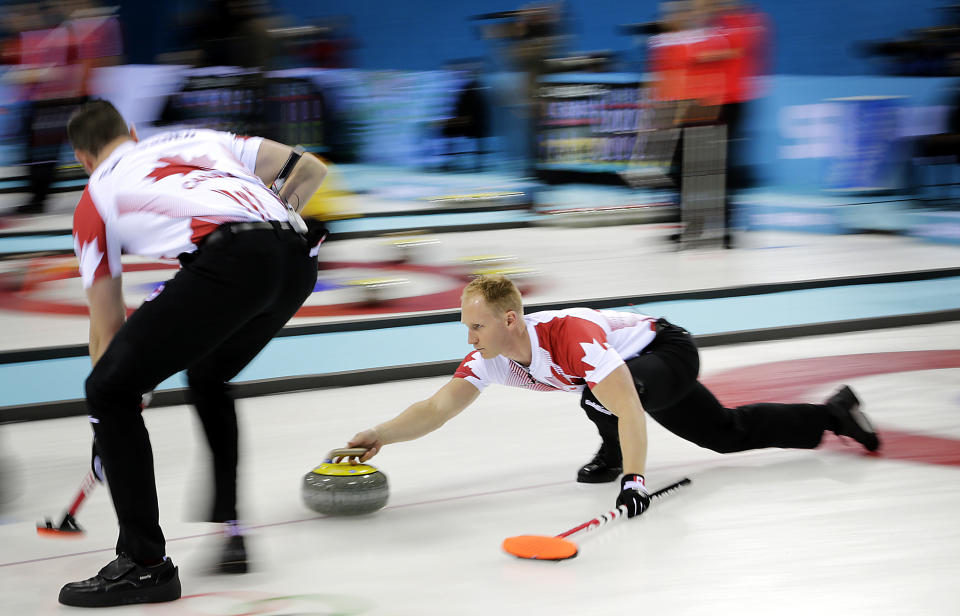 Canada's skip Brad Jacobs, right, delivers the rock while his teammate Ryan Harnden, Left, prepares to sweep the ice during the men's curling competition against Germany at the 2014 Winter Olympics, Monday, Feb. 10, 2014, in Sochi, Russia. (AP Photo/Wong Maye-E)