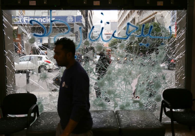 A man stands near a broken facade of a bank in Beirut