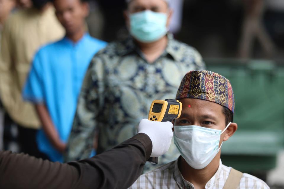 A security guard takes the body temperature of a Muslim worshipper amid fears of the new coronavirus outbreak, prior to the start of a Friday prayer at Al Akbar Mosque in Surabaya, on March 27.