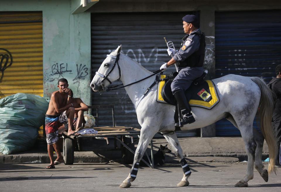 A military police officer rides a horse past residents during a police operation to occupy the Mare slum complex in Rio de Janeiro, Brazil, Sunday, March 30, 2014. The Mare complex of slums, home to about 130,000 people and located near the international airport, is the latest area targeted for the government's "pacification" program, which sees officers move in, push out drug gangs and set up permanent police posts. (AP Photo/Leo Correa)