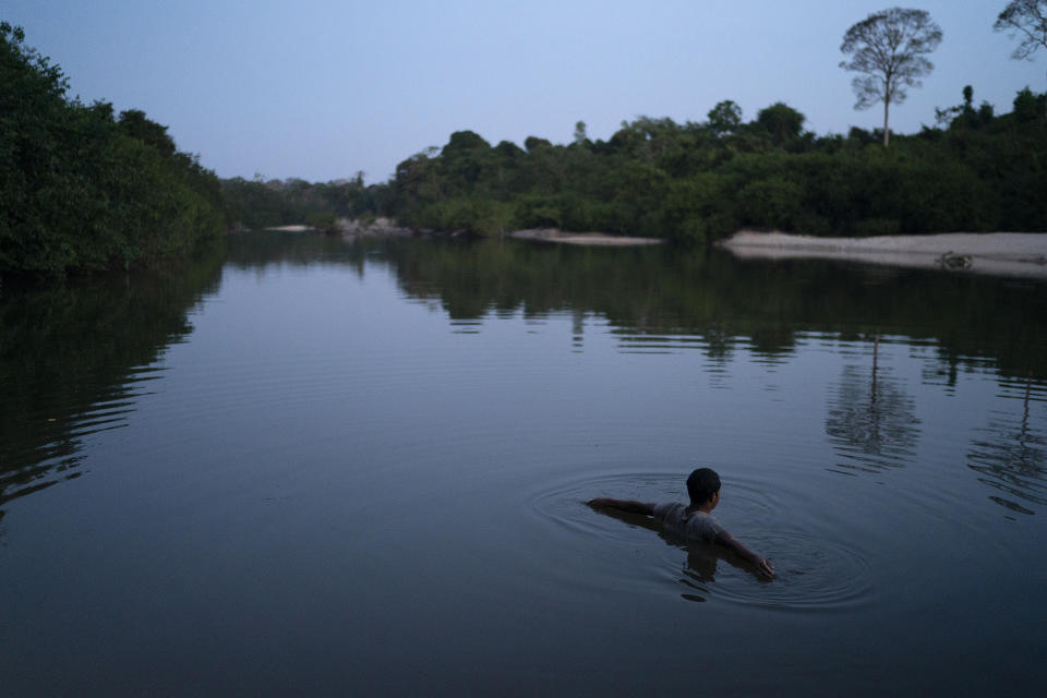 In this Aug. 26, 2019 photo, a youth from the Kayapo indigenous community bathes in the river at dusk near his village in the Bau indigenous reserve in Altamira in Brazil's Amazon. President Jair Bolsonaro has long pushed to open indigenous reserves for agriculture and mining, saying it will benefit the people there. He insists Brazil’s indigenous people, “want to integrate, they want electricity, they want to be what we are.” (AP Photo/Leo Correa)