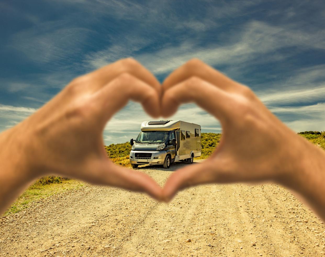 Motorhome on a dust road with a heart shaped human hand