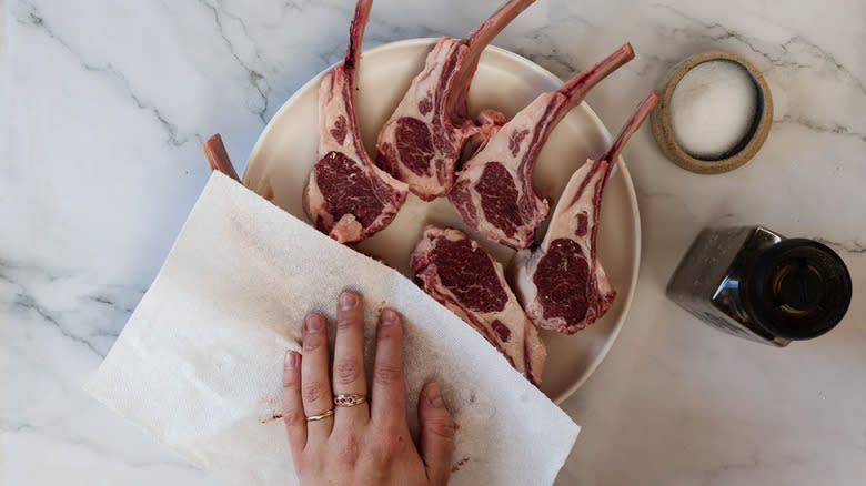 Patting lamb chops with paper towel