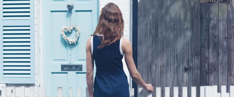 A young woman is looking at a little house with a blue door