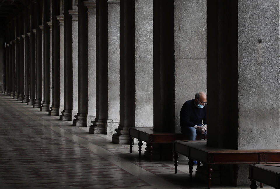 In this picture taken on Wednesday, May 13, 2020, a man wearing a sanitary mask sits in St. Mark's Square in Venice, Italy. Venetians are rethinking their city in the quiet brought by the coronavirus pandemic. For years, the unbridled success of Venice's tourism industry threatened to ruin the things that made it an attractive destination to begin with. Now the pandemic has ground to a halt Italy’s most-visited city, stopped the flow of 3 billion euros in annual tourism-related revenue and devastated the city's economy. (AP Photo/Antonio Calanni)