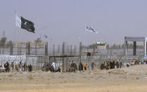 FILE - Pakistan and Taliban flags flutter on their respective sides while people walk through a security barrier to cross border at a key border crossing point between Pakistan and Afghanistan, in Chaman, Pakistan, Aug. 18, 2021. The Taliban win in Afghanistan gave a boost to militants in neighboring Pakistan. Faced with rising violence, Pakistan is taking a tougher line to pressure Afghanistan’s Taliban rulers to crack down on militants hiding on their soil, but so far the Taliban remain reluctant to take action -- trying instead to broker a peace. (AP Photo/Jafar Khan, File)