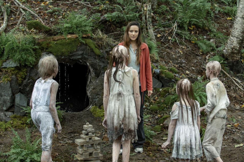 A woman is cornered by a cavern by a number of creepy, ghost-like children