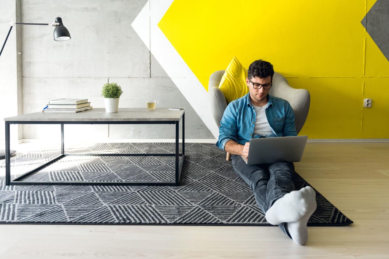 man working in hip living room on laptop while sitting on the floor