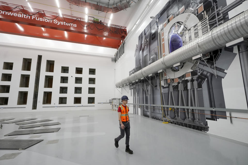 Alex Creely, head of Tokamak operations, walks past a life-sized representation, right, of a device that will use magnets to create the conditions for fusion to happen, Wednesday, Oct. 11, 2023, at Commonwealth Fusion Systems, in Devens, Mass. Commonwealth is trying to create fusion inside what's called a tokamak. Nuclear fusion, which would be a new source of carbon-free energy, melds two hydrogen atoms together to produce a helium atom and a lot of energy. (AP Photo/Steven Senne)