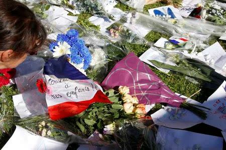 A woman is seen near flowers and a flag placed in tribute to victims two days after an attack by the driver of a heavy truck who ran into a crowd on Bastille Day killing scores and injuring as many on the Promenade des Anglais, in Nice, France, July 16, 2016. REUTERS/Pascal Rossignol