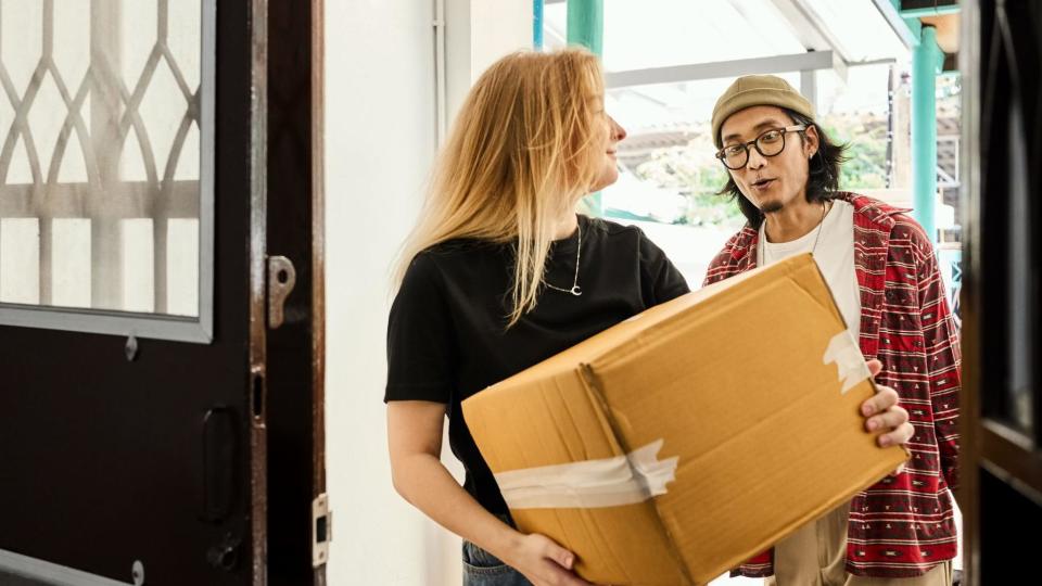 Young couple carrying boxes through a doorway while moving in together into a new building