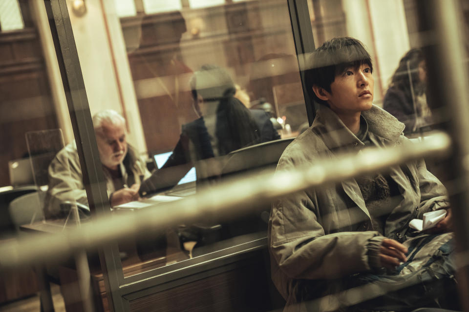 a man (Song Joong-ki as Loh Kiwan) sits in front of a mirror showing the reflection of a white-haired man and black-haired woman at a desk